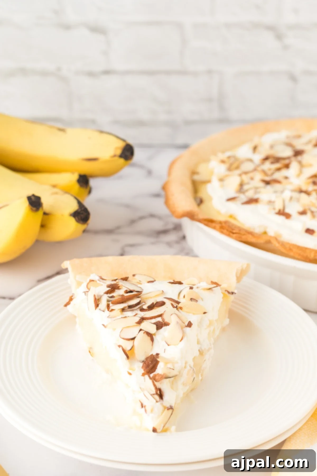 Creamy Banana Delight 2 slice of banana cream pie on a plate with almonds on top and bananas on a table