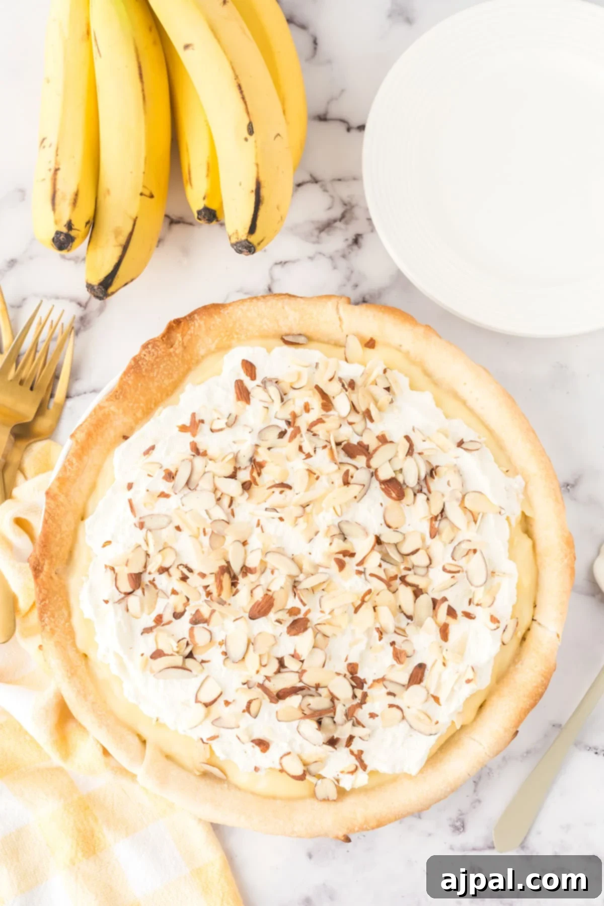 Creamy Banana Delight 12 banana cream pie in a pie plate with almonds on top and bananas on a table