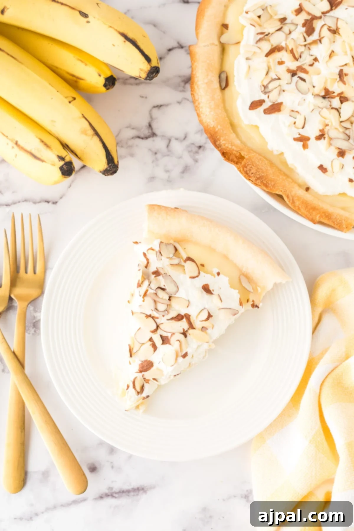 Creamy Banana Delight 13 slice of banana cream pie on a plate with almonds on top and bananas on a table and a fork next to it