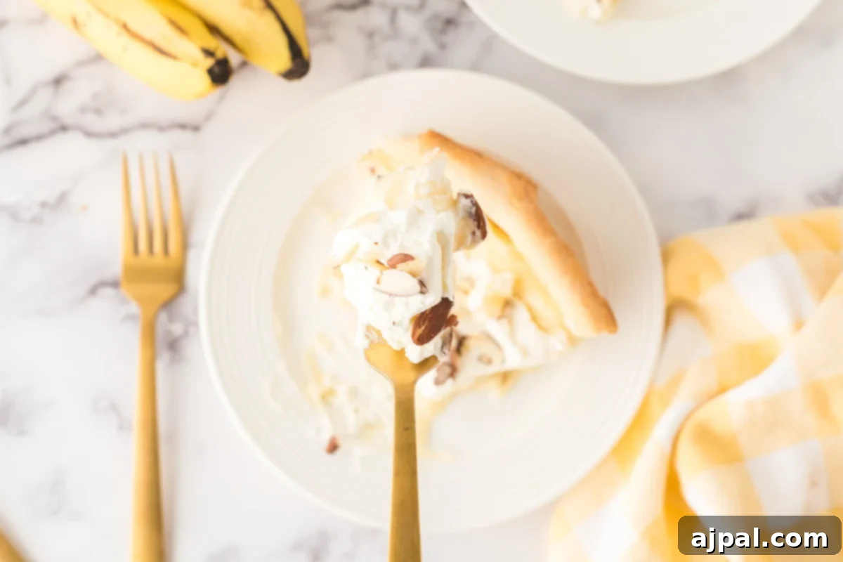 Creamy Banana Delight 3 a bit of banana cream pie on a fork held over a slice of banana cream pie on a plate with almonds on top and bananas on a table