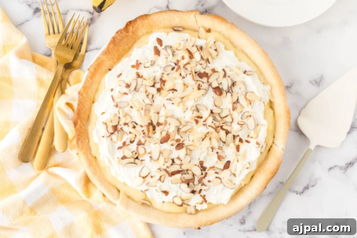 Creamy Banana Delight 14 slice of banana cream pie on a plate with almonds on top and bananas on a table with a pie knife next to it