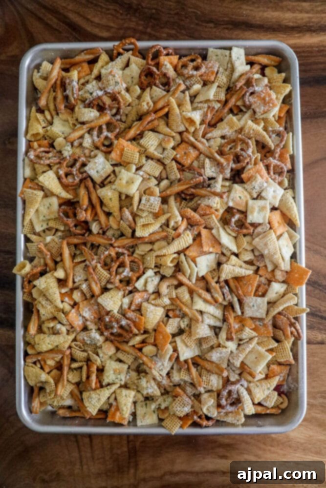 Ranch-seasoned Chex Mix, with its delightful blend of crackers and pretzels, spread out evenly on a baking sheet, ready for baking.