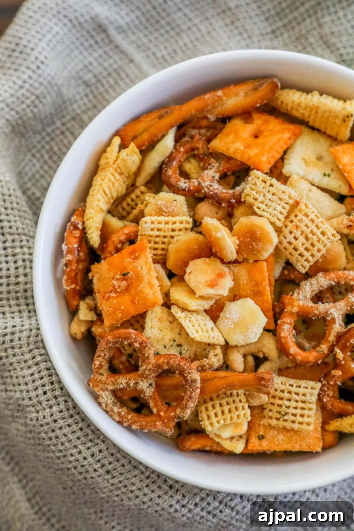 A white bowl brimming with homemade Ranch Chex Mix, featuring crunchy nuts and savory pretzels among the seasoned crackers.
