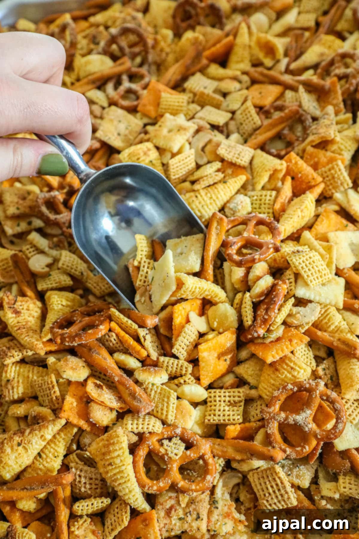A hand scooping a generous portion of freshly seasoned ranch Chex Mix from a large bowl, showcasing its crunchy texture and even seasoning.