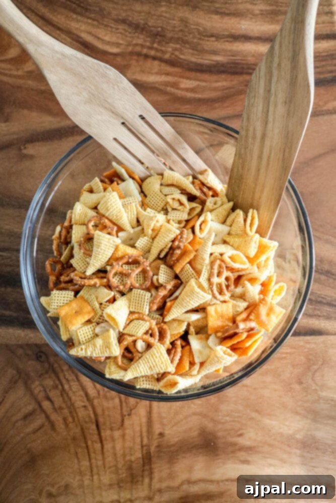 Two wooden forks in a bowl, actively tossing Chex mix and ranch seasoning to ensure a uniform coating on all ingredients.