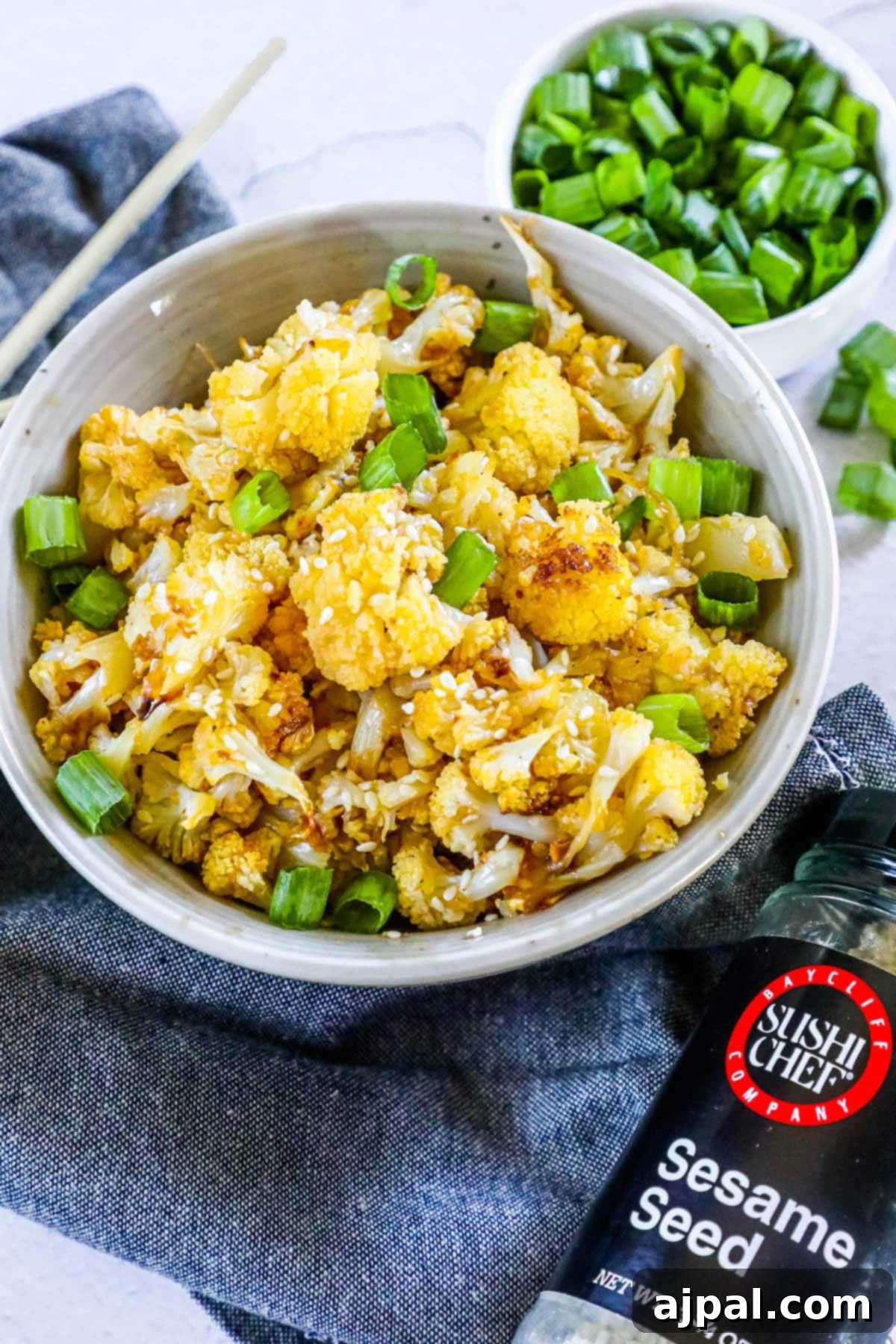 A bowl of sweet and spicy baked cauliflower, perfectly glazed and topped with toasted sesame seeds, photographed on a wooden table.