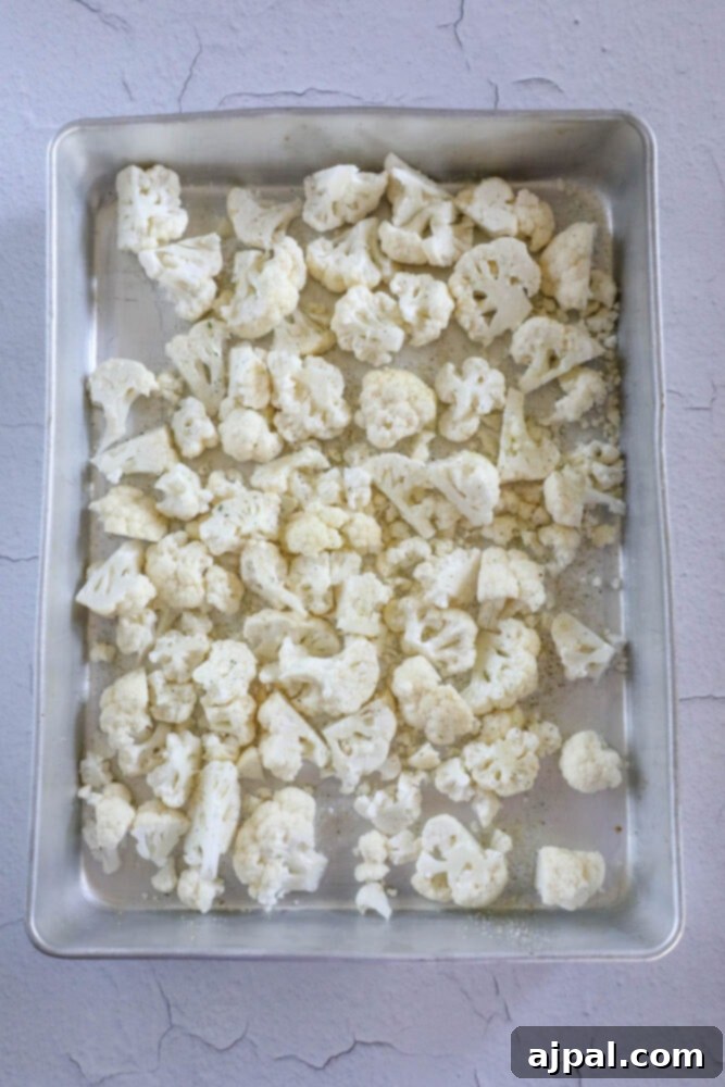 Raw cauliflower florets are evenly spread on a baking sheet lined with aluminum foil, prepared for roasting.