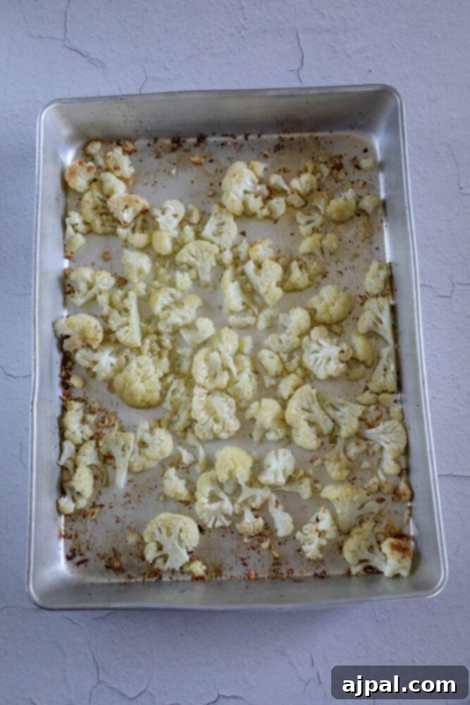 Golden-brown roasted cauliflower florets are scattered on a baking sheet lined with aluminum foil, indicating they are perfectly cooked and ready for the sauce.