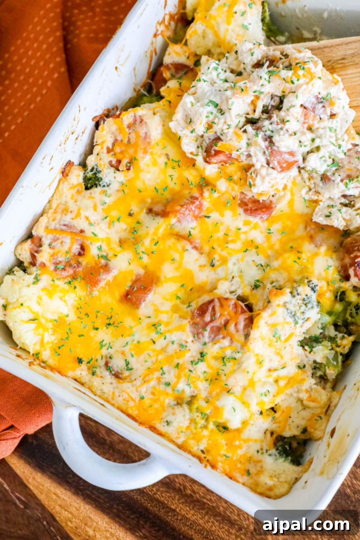 A vibrant cheesy casserole featuring sliced sausage, tender broccoli florets, and white cauliflower, beautifully seasoned with herbs, served in an elegant white baking dish on a rustic wooden table.