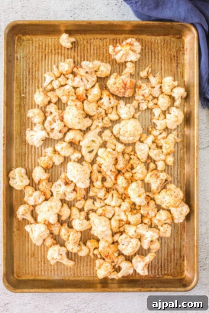 raw cauliflower tossed in spices on a baking sheet