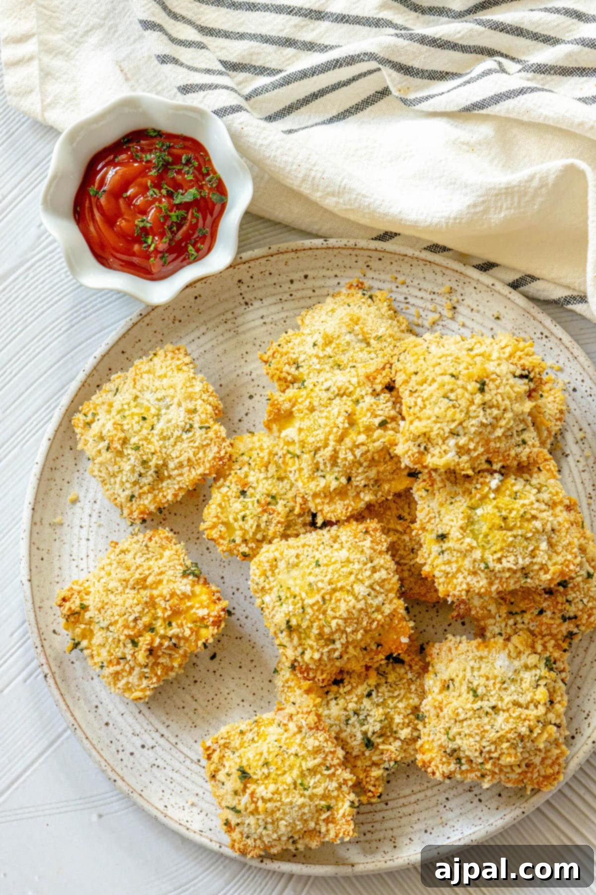 Crunchy baked breaded ravioli on a white speckled plate with a small bowl of ketchup next to it