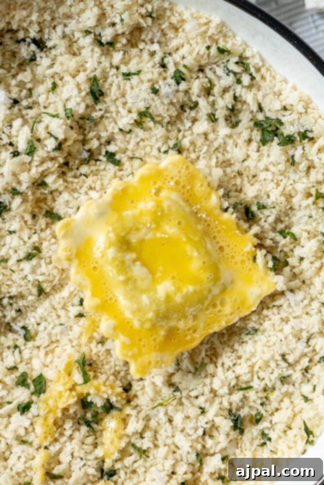 Egg-coated ravioli being dipped into a bowl of Italian seasoned breadcrumbs and Parmesan cheese