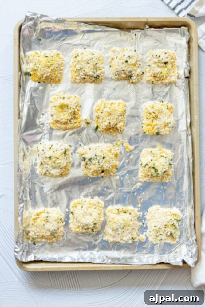 Breaded raviolis arranged neatly on a baking sheet lined with parchment paper