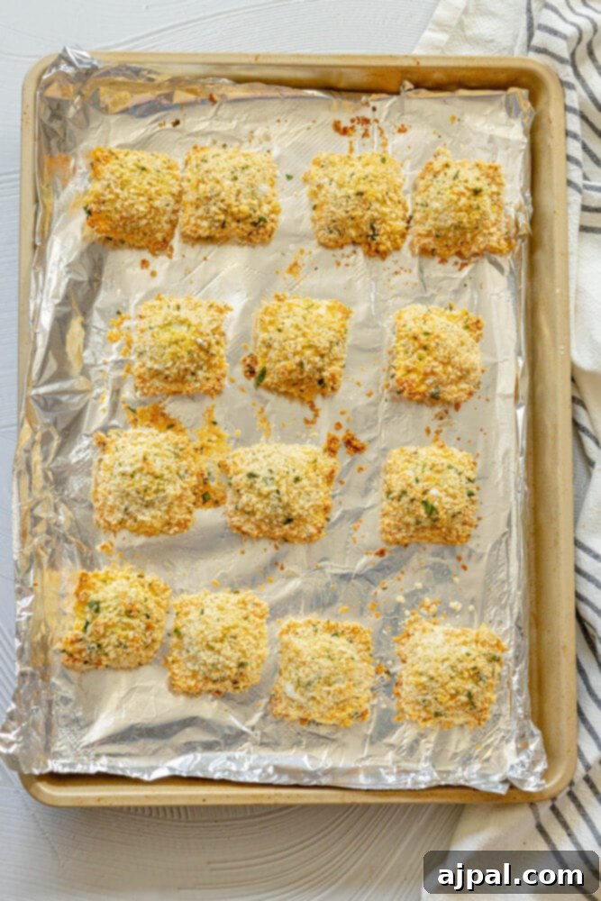 Crispy, golden-brown baked breaded ravioli on a baking sheet, fresh out of the oven