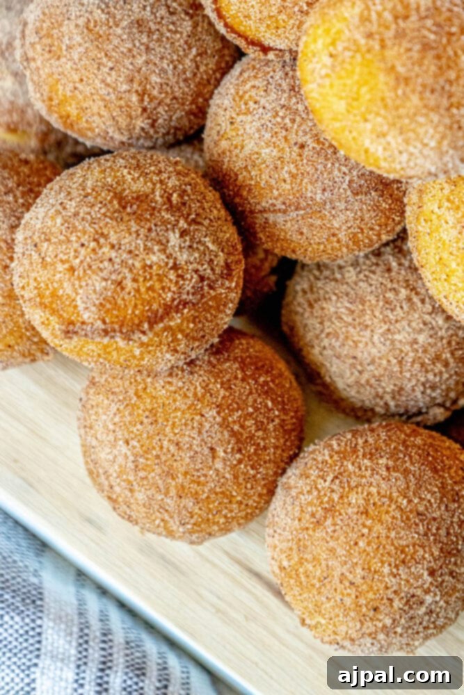 A beautiful stack of golden-brown cinnamon sugar donut holes arranged on a rustic wooden cutting board, glistening with sweet spice.