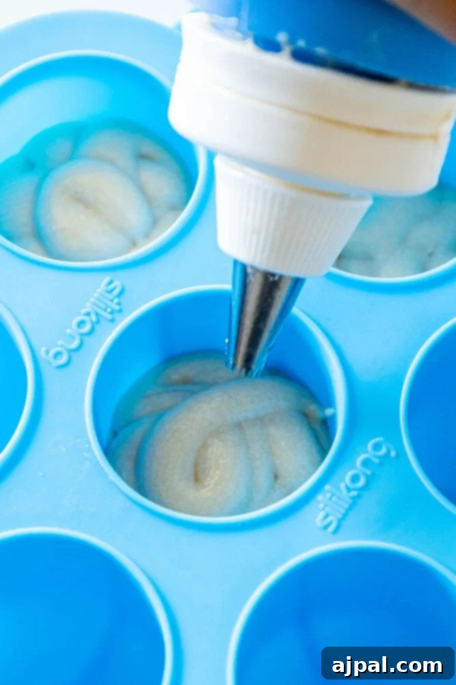 A hand expertly piping soft batter into the round molds of a donut hole pan, ensuring even portions.