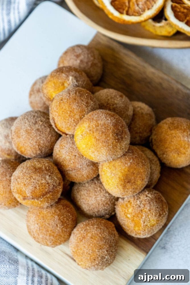 A beautifully arranged stack of cinnamon sugar donut holes, garnished with a sprig of fresh mint, on a wooden cutting board.