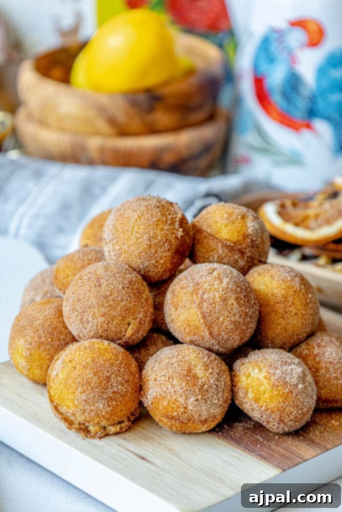 A generous pile of freshly baked cinnamon sugar donut holes creating a mouth-watering display on a light-colored wooden cutting board.