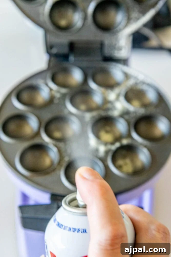 A nonstick spray being applied to a cake pop machine, ensuring easy release of the baked donut holes.