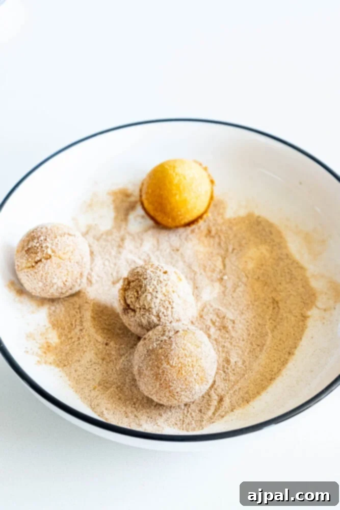 Freshly baked donut holes being rolled and coated in a generous layer of cinnamon sugar in a bowl.