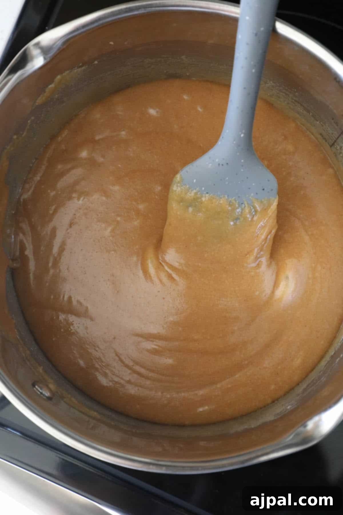 A brown sauce in a pan being stirred with a spatula, resembling the texture of scotcheroos.