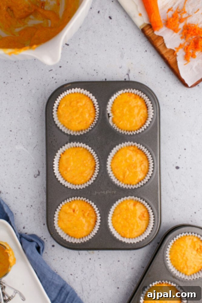 Effortless Carrot Muffins 11 Muffin batter has been neatly scooped into cupcake liners, nestled within a muffin tin on a kitchen table, awaiting baking.