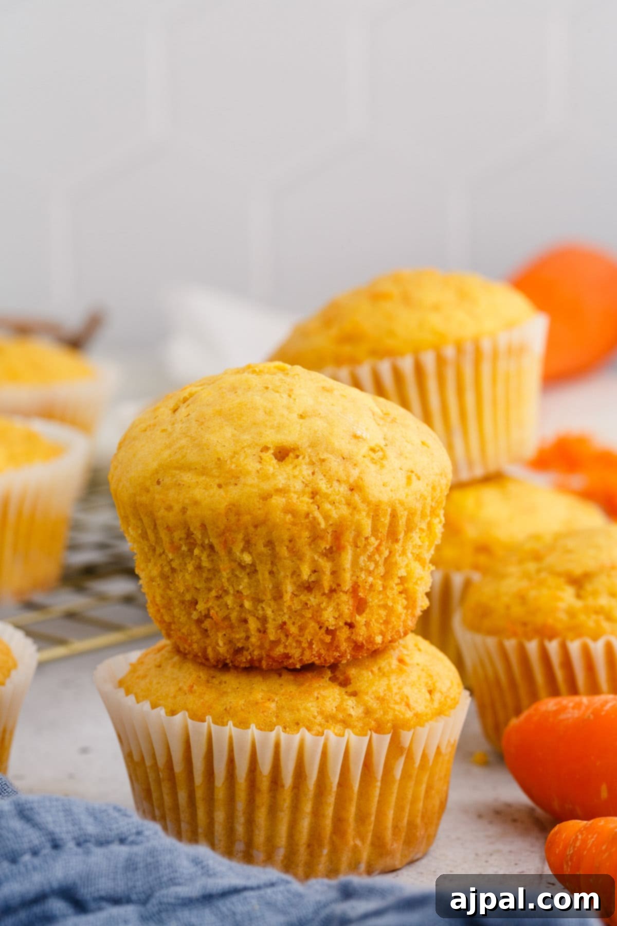 Effortless Carrot Muffins 13 Freshly baked carrot muffins are gently stacked on top of each other on a table, creating an appealing display.