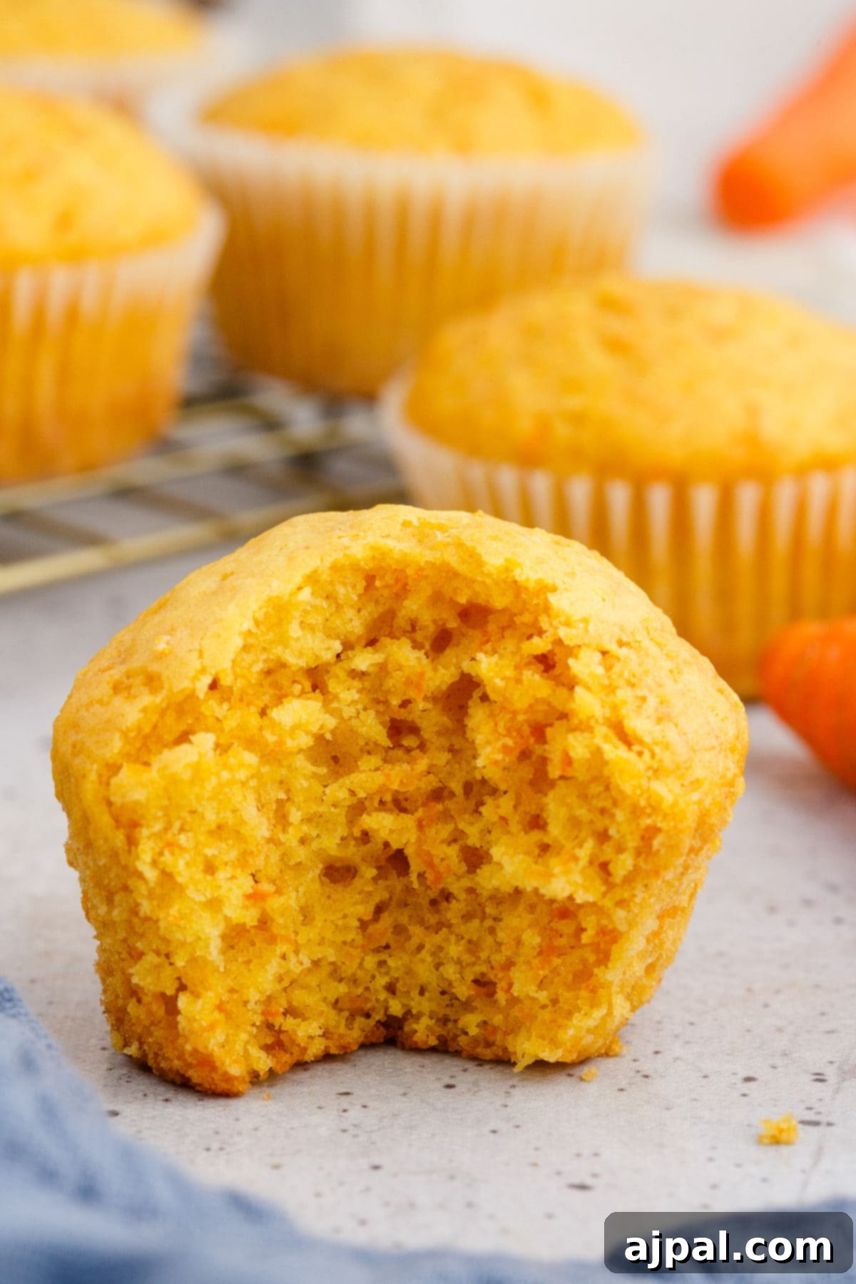 Effortless Carrot Muffins 4 A baked carrot muffin with a large bite taken out, revealing its light, airy, and moist interior texture.