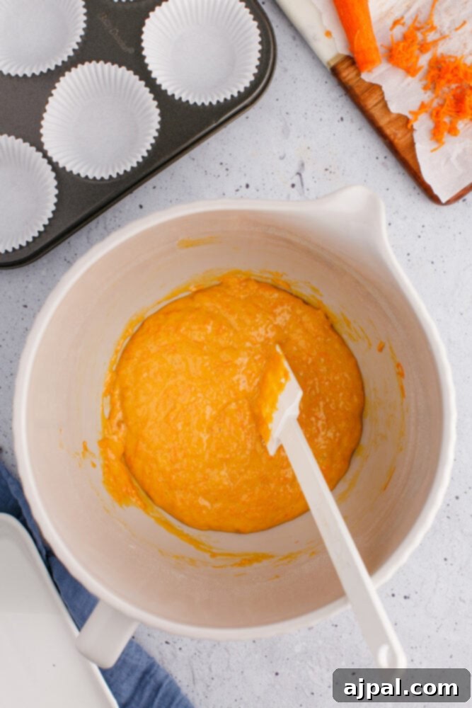 Effortless Carrot Muffins 9 The mixed carrot muffin batter in a bowl, with a plastic stirrer resting, showcasing its consistent and inviting texture.