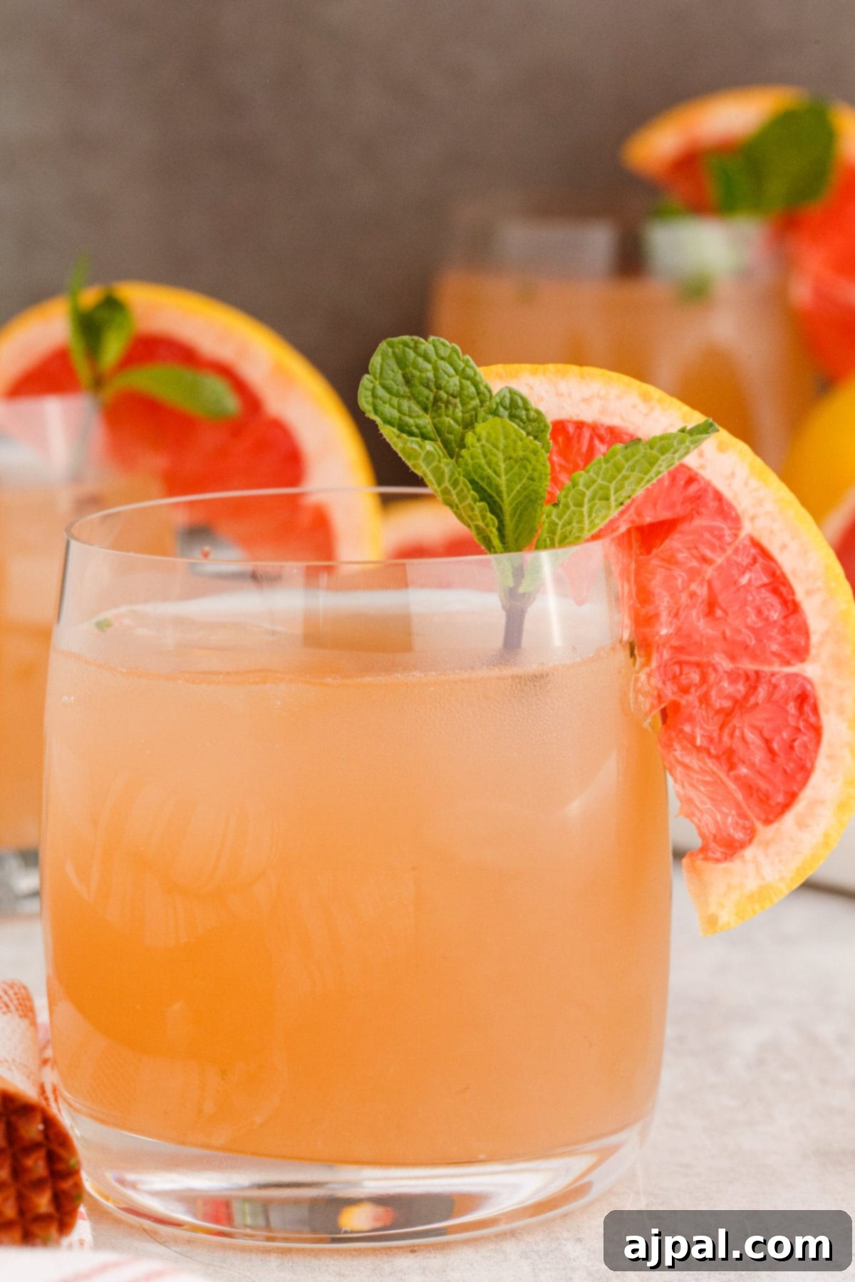 grapefruit mojito cocktail in a short glass with a sprig of mint and a slice of grapefruit on the side