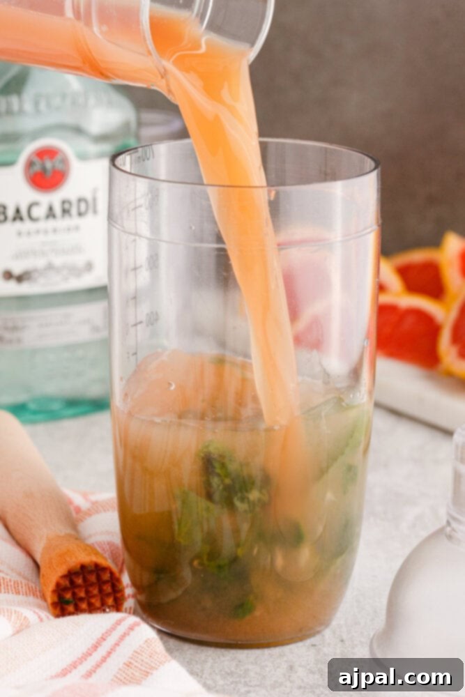 pouring grapefruit juice into a cocktail shaker with rum, sugar, and mint