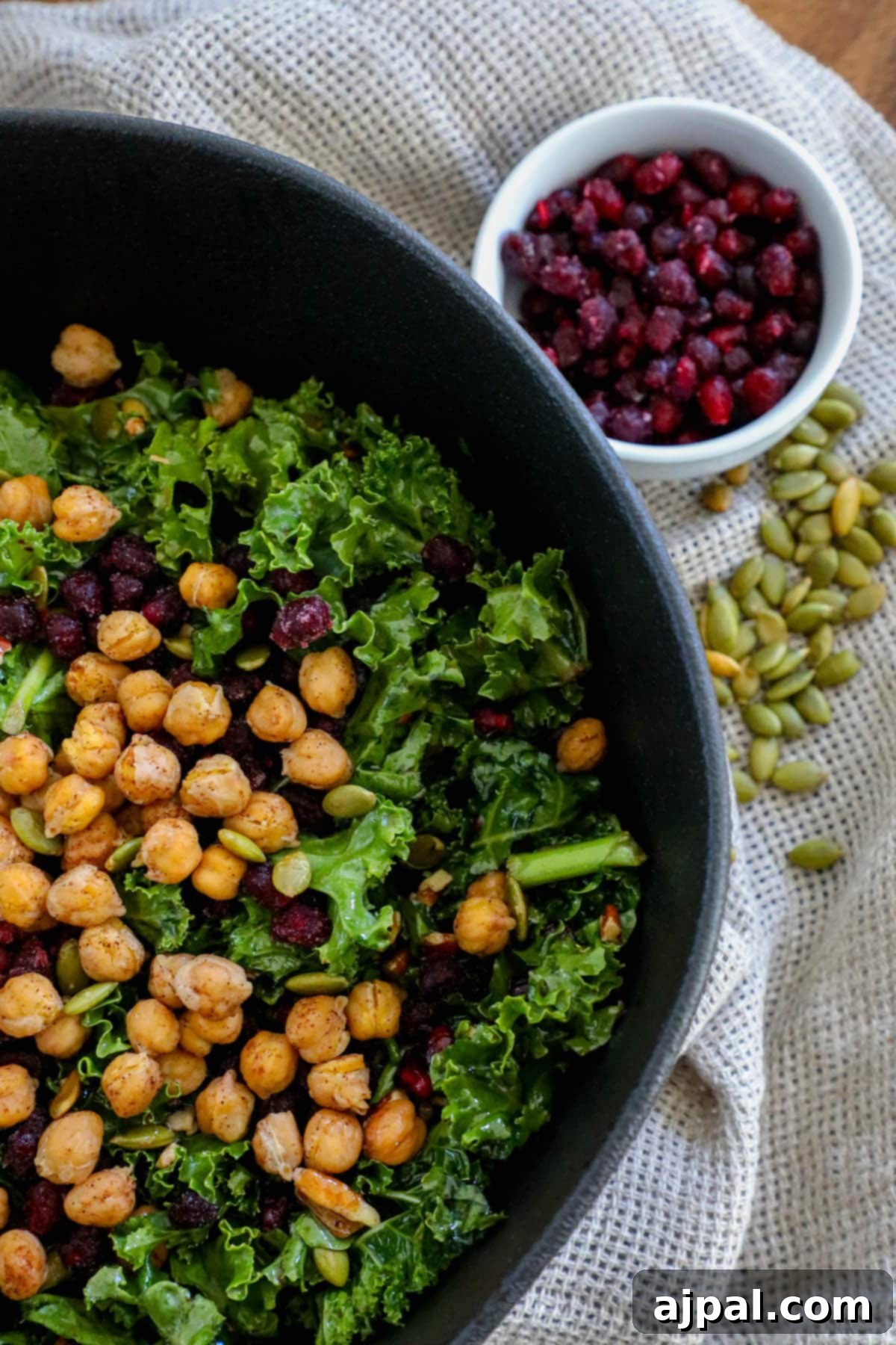 Jeweled Chickpea Pomegranate Salad 10 kale salad in a bowl with chickpeas, dried cranberries, pomegranate arils, pepitas, and dressing