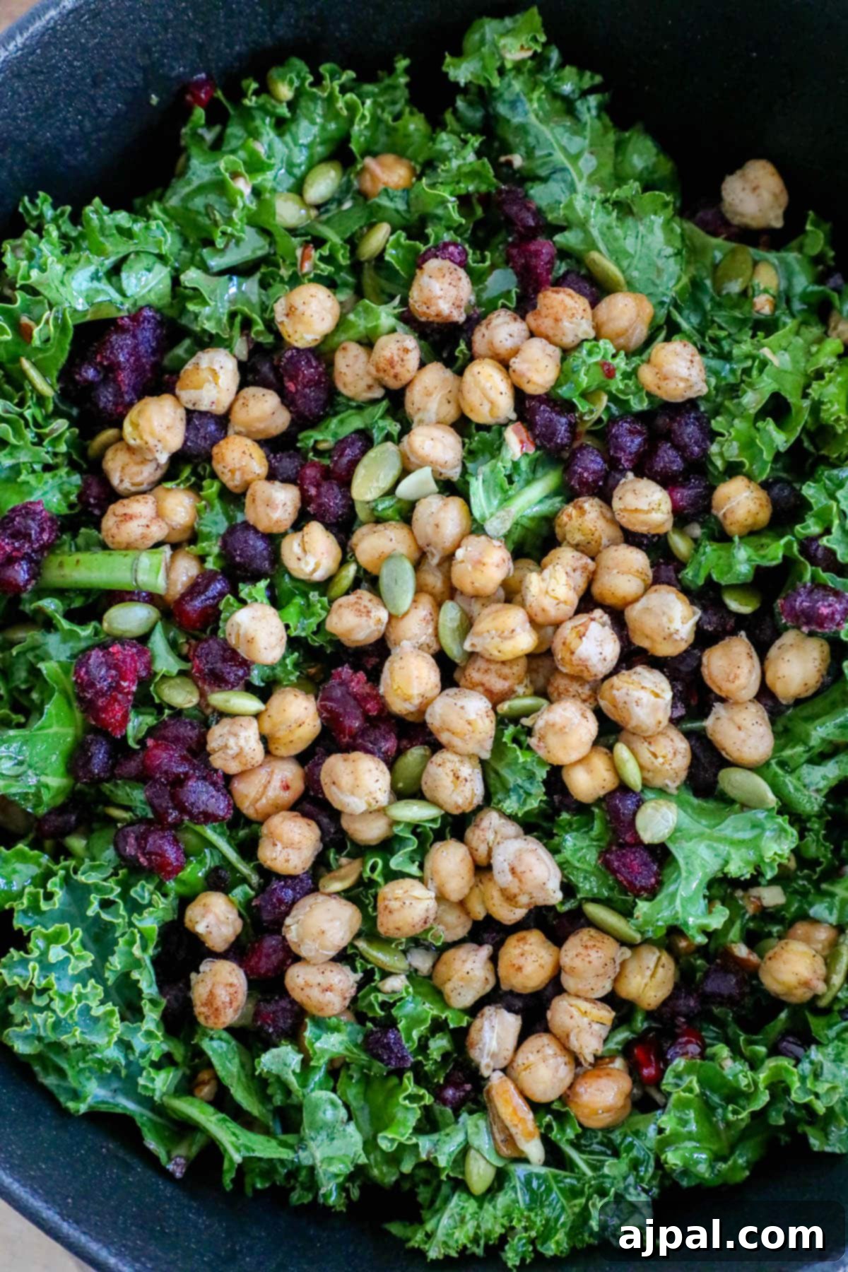 Mediterranean Chickpea Pomegranate Salad 3 Kale salad in a bowl with chickpeas, dried cranberries, pomegranate arils, pepitas, and dressing