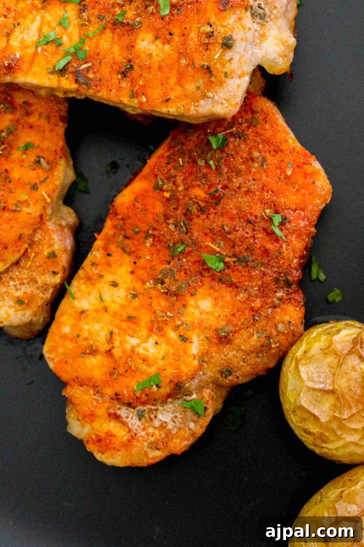 Zesty Ranch Pork Chops and Roasted Potatoes 9 browned seasoned pork chops on a black plate next to a bottle of ranch dressing seasoning