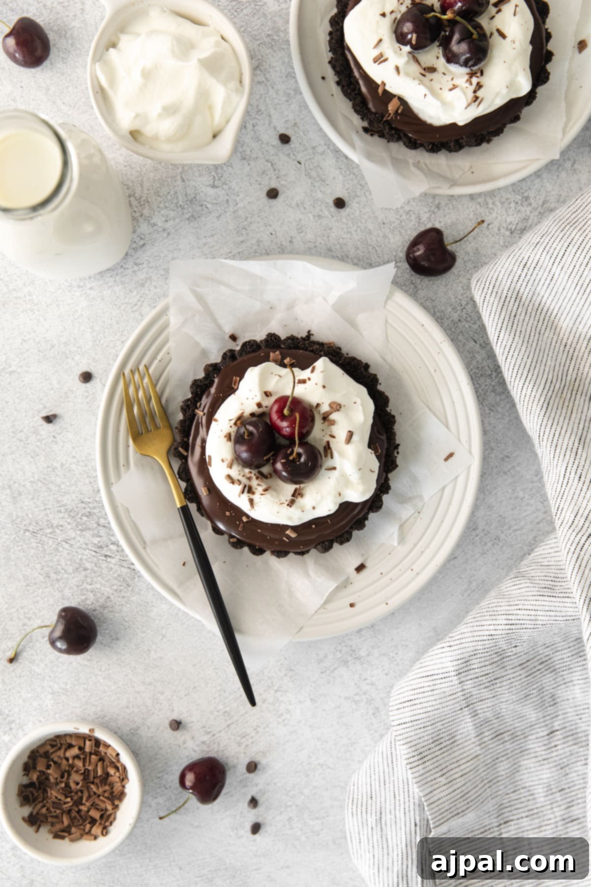 Dark Forest Cherry Delights 2 A beautifully plated Black Forest tart featuring a dark chocolate crust, topped with swirls of white whipped cream and garnished with fresh, glistening red cherries. A gold and black fork rests beside the plate, hinting at the decadent experience awaiting.