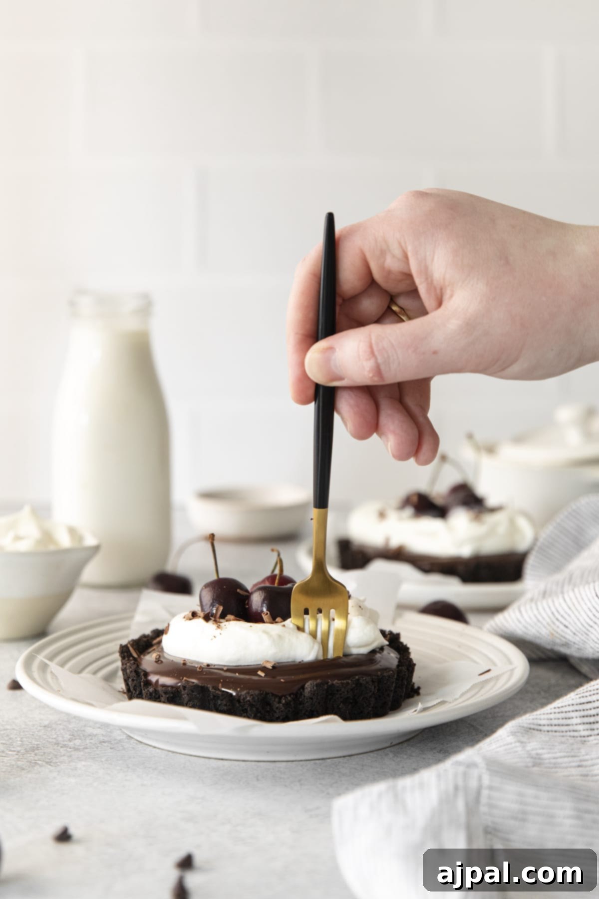 Dark Forest Cherry Delights 11 A hand gently pushes a fork into a decadent Black Forest tart, revealing the layers of chocolate ganache and Oreo crust, crowned with fluffy whipped cream and fresh cherries.