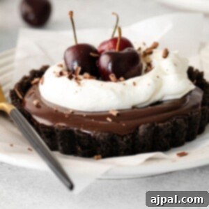 Dark Forest Cherry Delights 13 A tempting Black Forest tart on a white plate, showcasing a crispy chocolate Oreo crust, a smooth chocolate ganache, and a vibrant topping of whipped cream and fresh cherries. A fork lies nearby, inviting one to indulge.