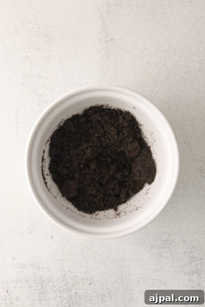 Dark Forest Cherry Delights 5 A close-up of dark, finely crushed Oreo crumbs in a bowl, showcasing their fine texture and readiness for use as a tart crust base.