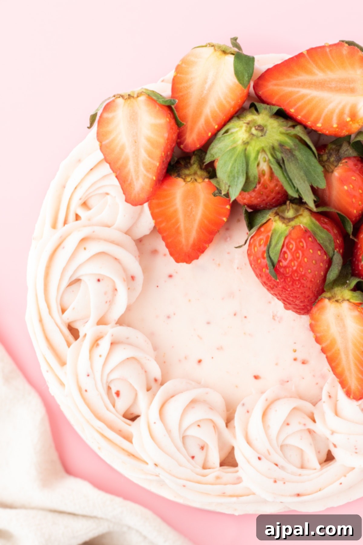 Fresh Strawberry Layer Cake 3 fresh sliced strawberries on top of a pink frosted cake with swirls of pink whipped icing on top