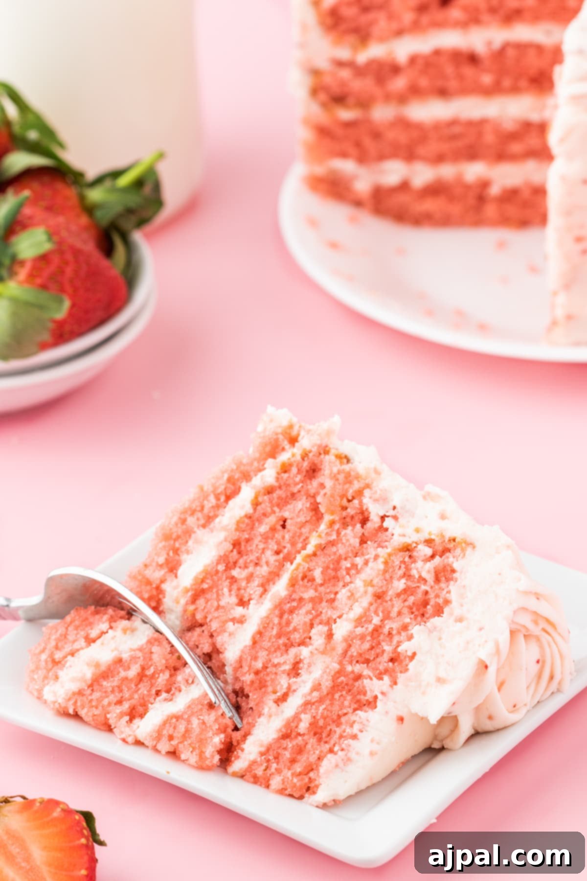 Fresh Strawberry Layer Cake 4 fresh sliced strawberries on a pink frosted cake with layers of whipped pink icing that has strawberry bits in it