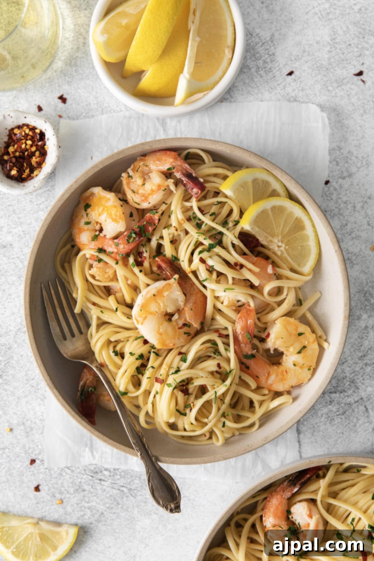 Effortless Shrimp Scampi 2 shrimp pasta with linguine, red pepper flakes, herbs, and lemon slices in a bowl with a fork in it