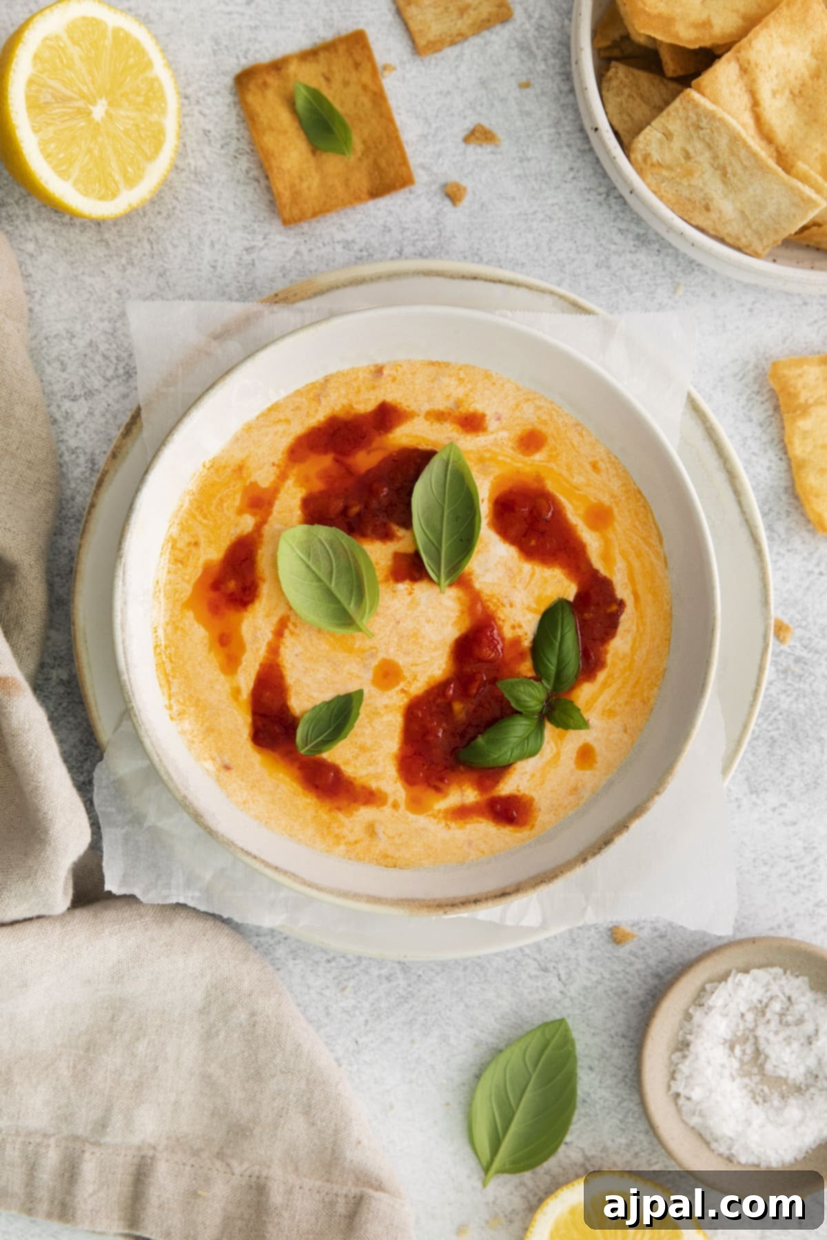 A bowl of creamy whipped feta with beautiful swirls of harissa paste, garnished with fresh basil leaves.