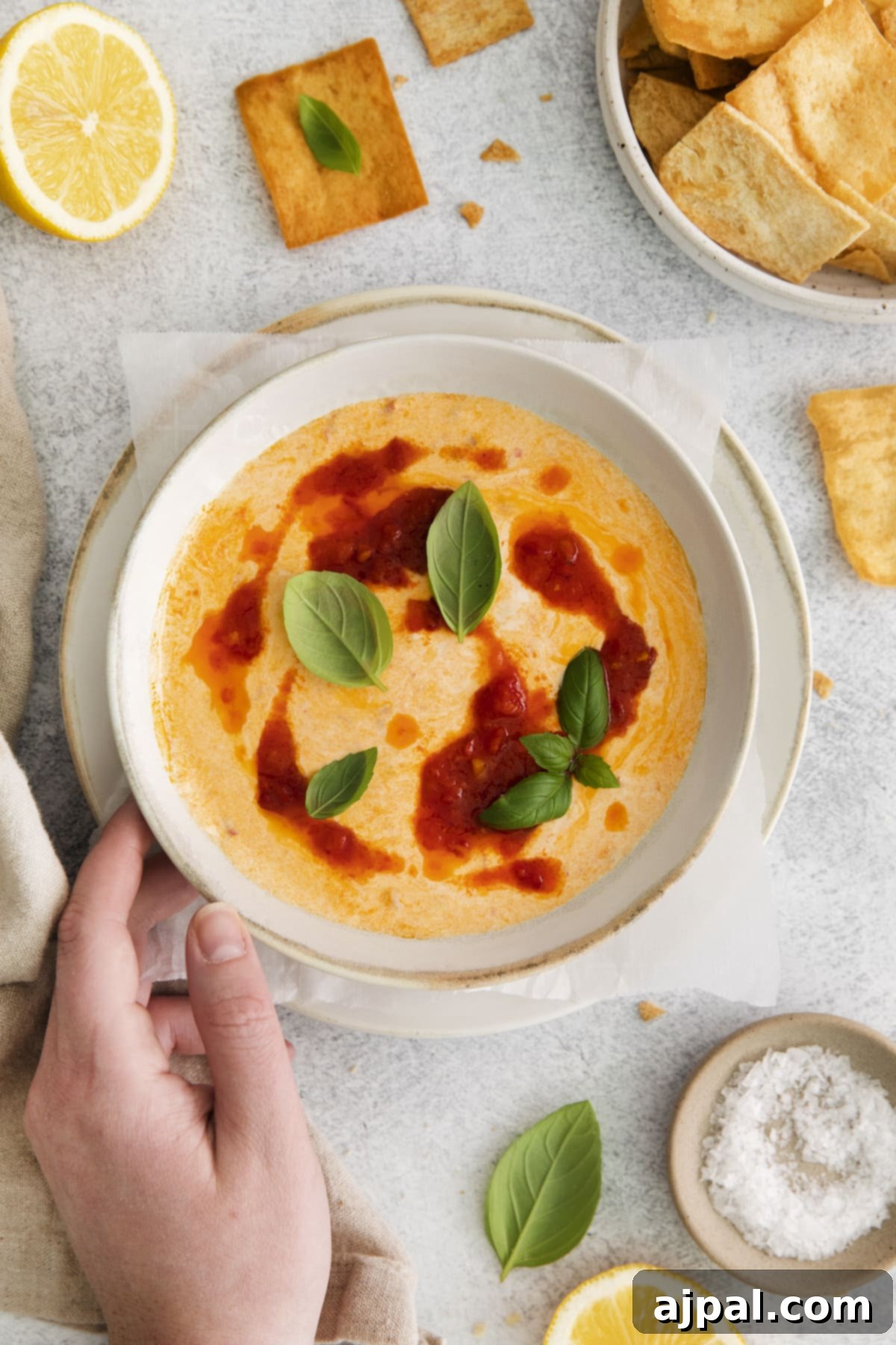 Close-up of whipped feta in a bowl with sprigs of basil on top and distinct spoonfuls of rich harissa paste swirled into the creamy texture.