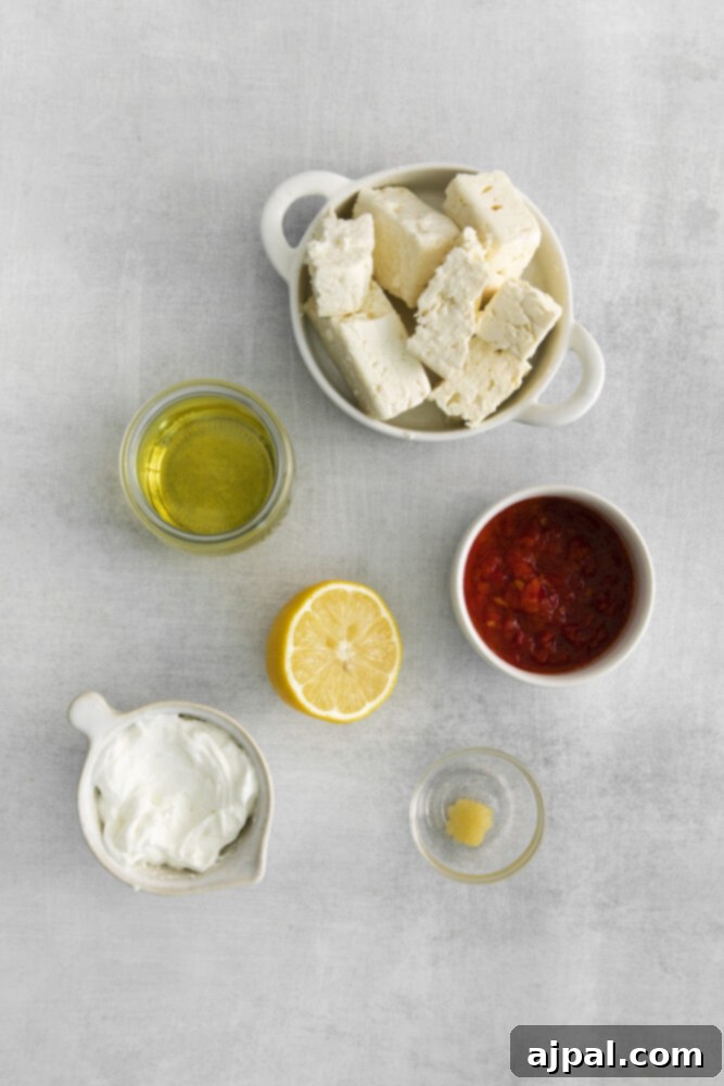 Fresh feta, olive oil, lemon, and garlic arranged on a white plate, highlighting the quality ingredients for the dip.