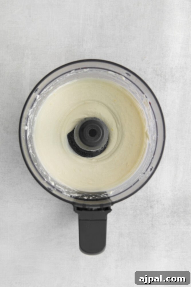 Smooth, blended feta and garlic mixture inside a food processor bowl, showcasing its creamy and airy consistency.