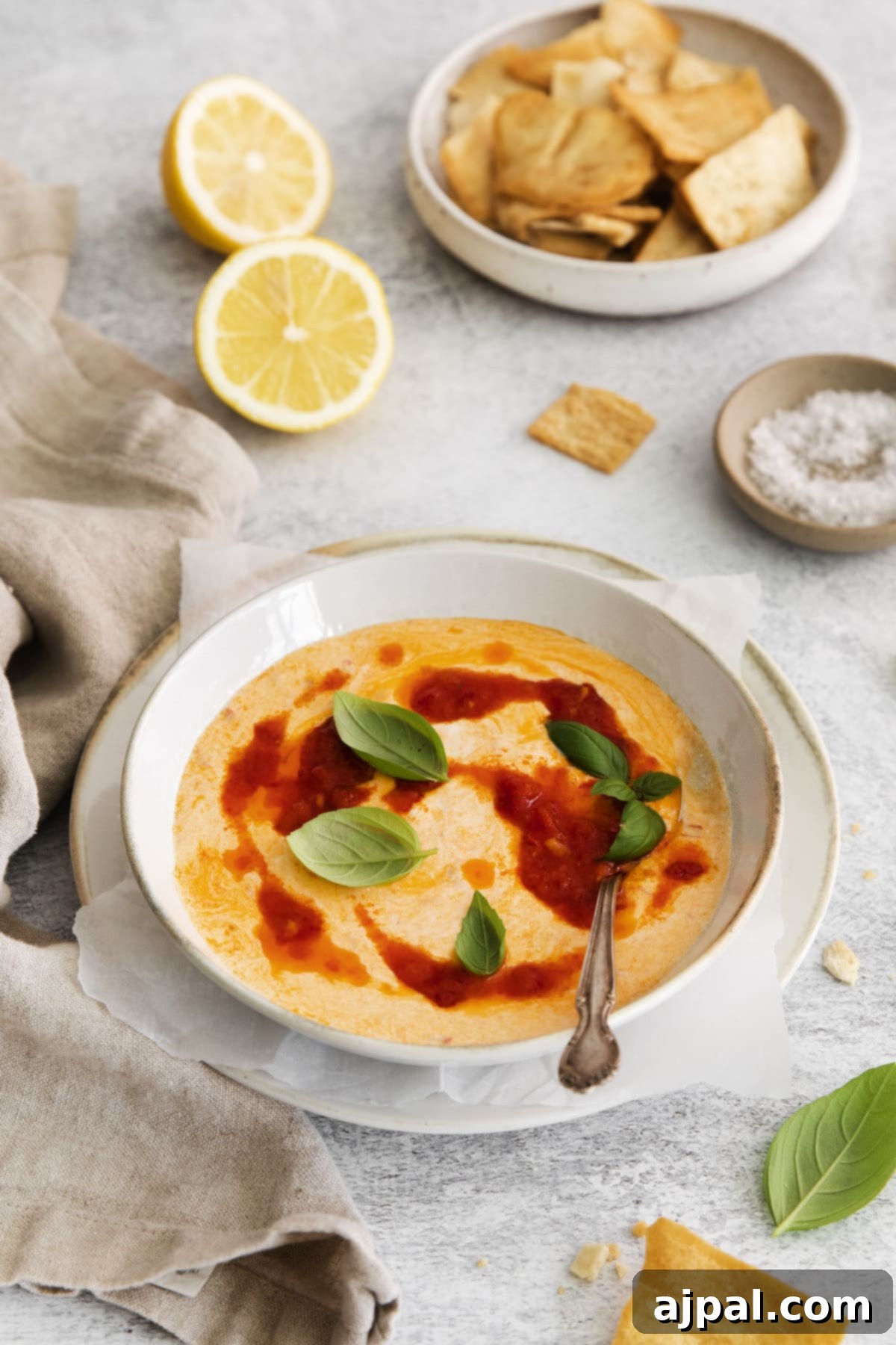A bowl of creamy whipped feta with beautiful swirls of harissa paste, garnished with fresh mint leaves and a spoon, inviting guests to dig in.