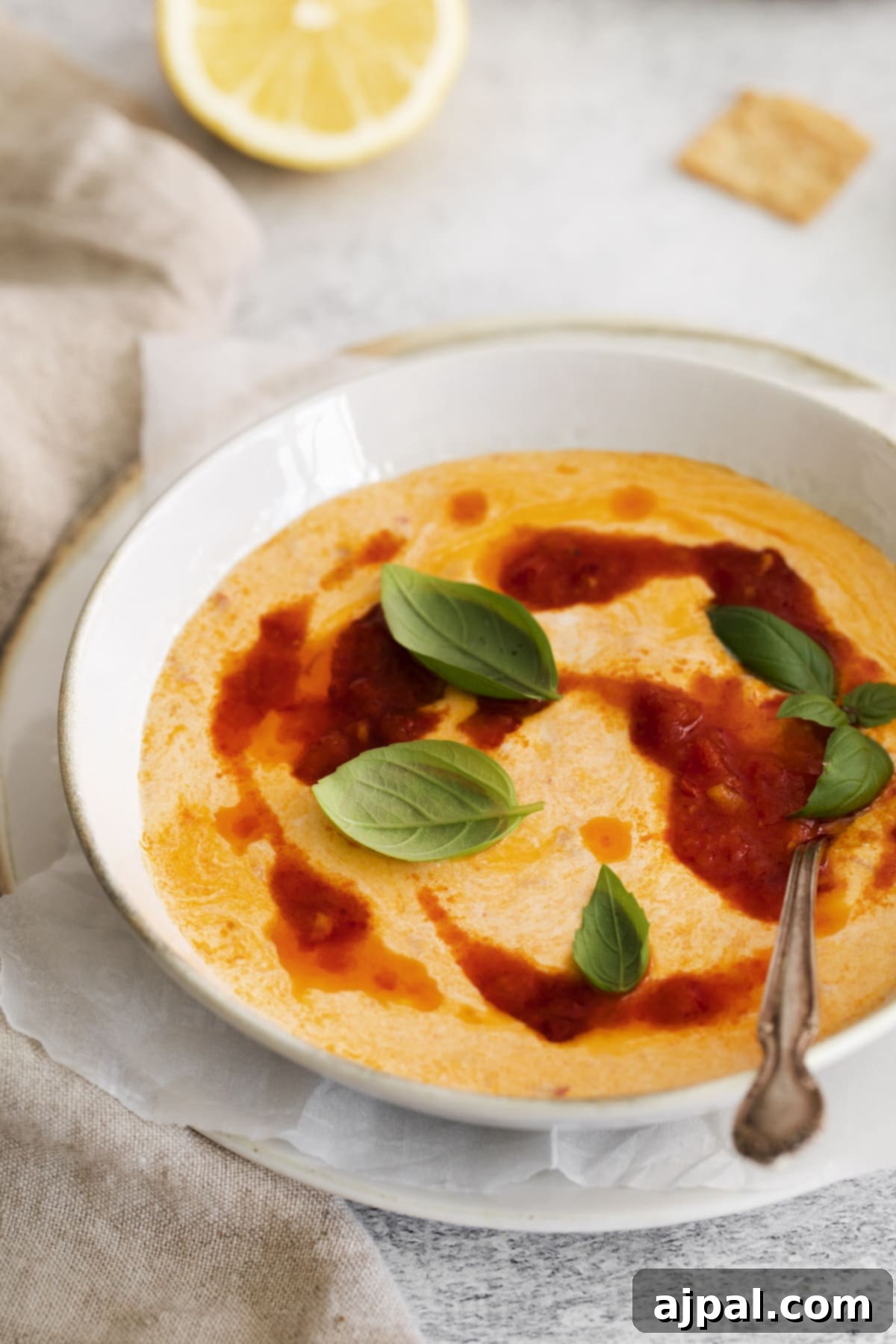 A beautifully presented bowl of harissa whipped feta with generous drizzles of spicy harissa oil and fresh basil, set on a rustic surface.