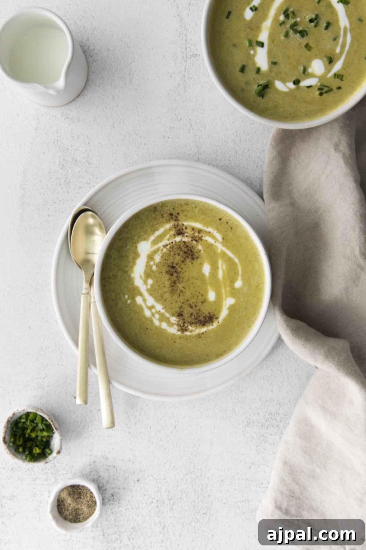 Velvety Instant Pot Asparagus Soup 3 creamy asparagus soup in a white bowl with a swirl of cream on top and lots of fresh cracked pepper next to a bowl of soup with chopped chives and cream on top