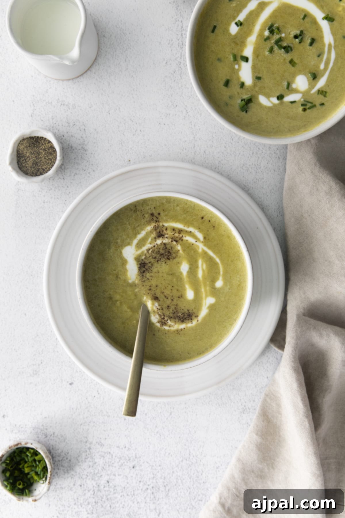 Velvety Instant Pot Asparagus Soup 4 a spoon in creamy asparagus soup in a white bowl with a swirl of cream on top and lots of fresh cracked pepper