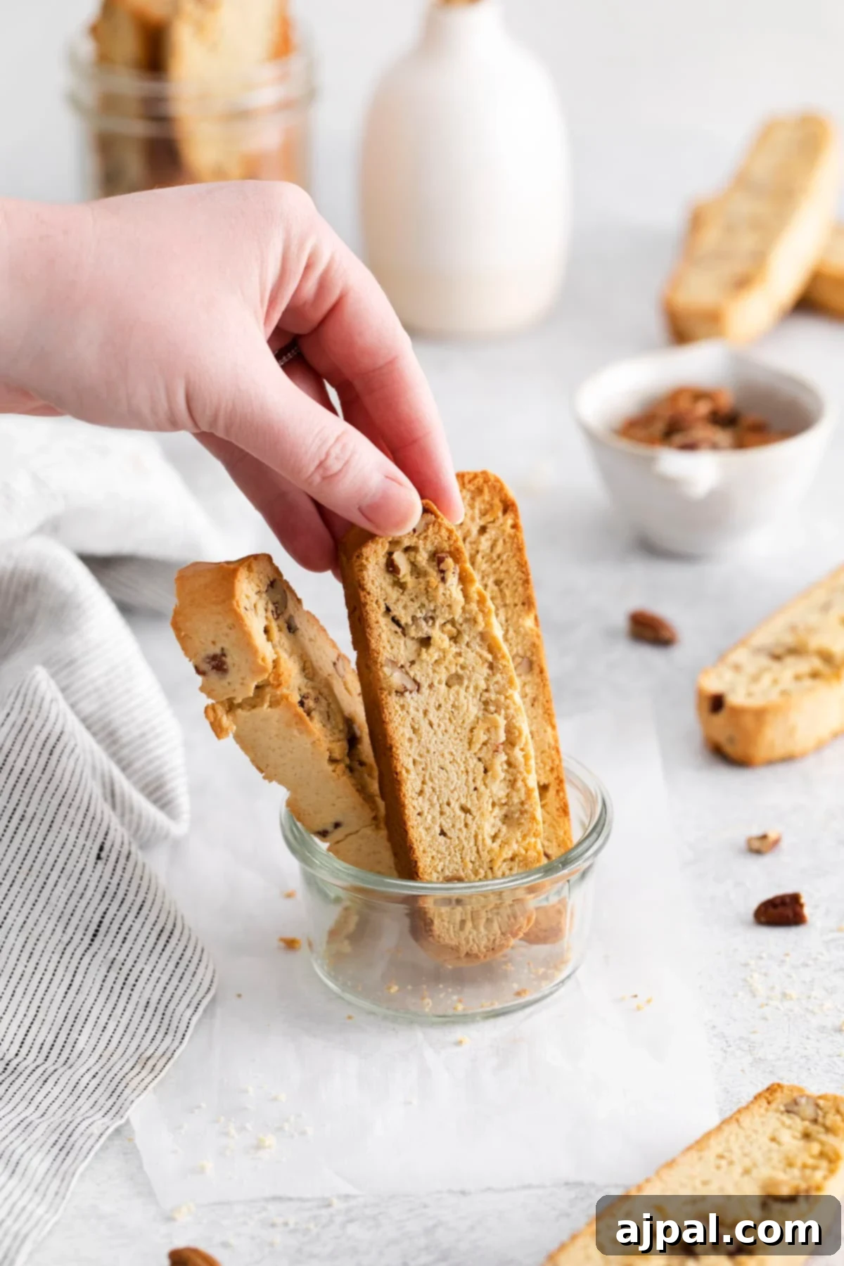 Artisan Maple Pecan Biscotti 11 A hand holding a biscotti in a jar on a table